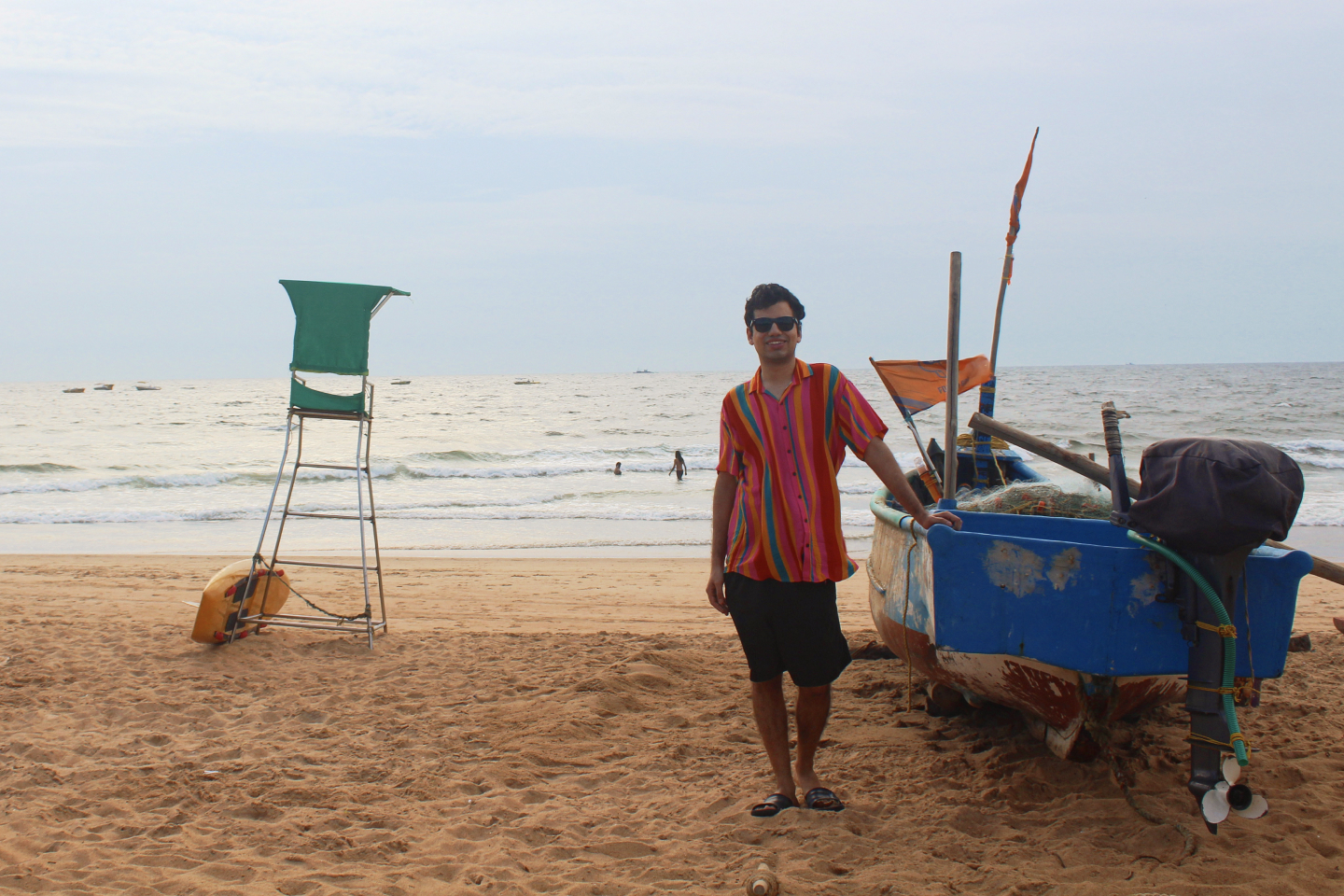 A man at the beach leaning against a boat