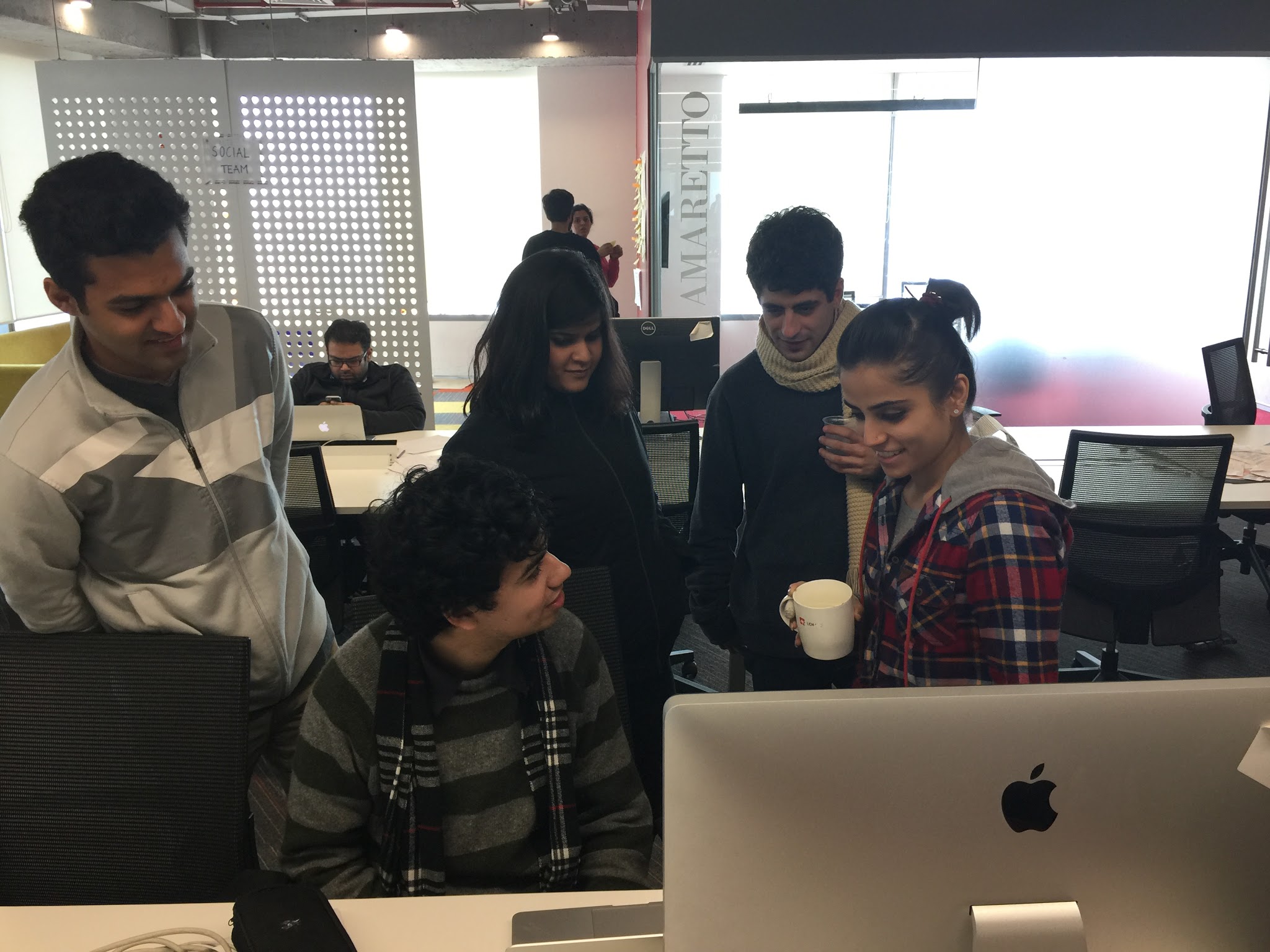 People hunched over a desk with a computer monitor and laptop on it.